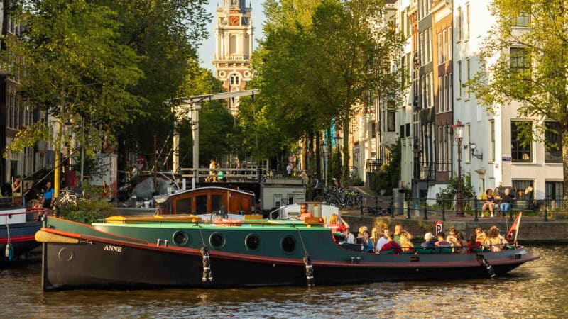 Klassischer Schlepper bei Sonnenuntergang auf den Amsterdamer Grachten mit einer Gruppe